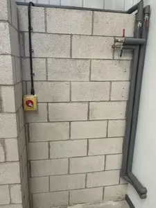 Bare block wall with existing pipes and electrical isolator before the wall-mounted pressure washer installation in Nottingham.